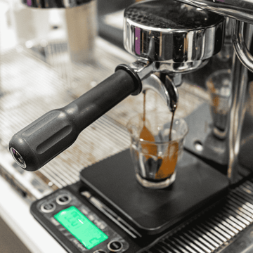 Espresso machine dispensing coffee into a glass on a digital scale.